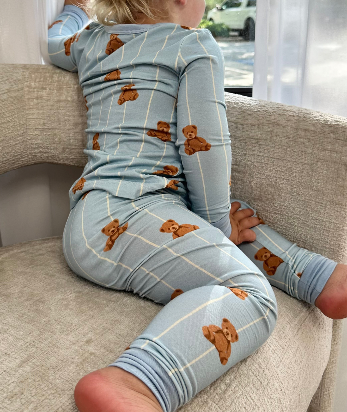 Child wearing a blue pajama set with teddy bear patterns sitting on a couch.